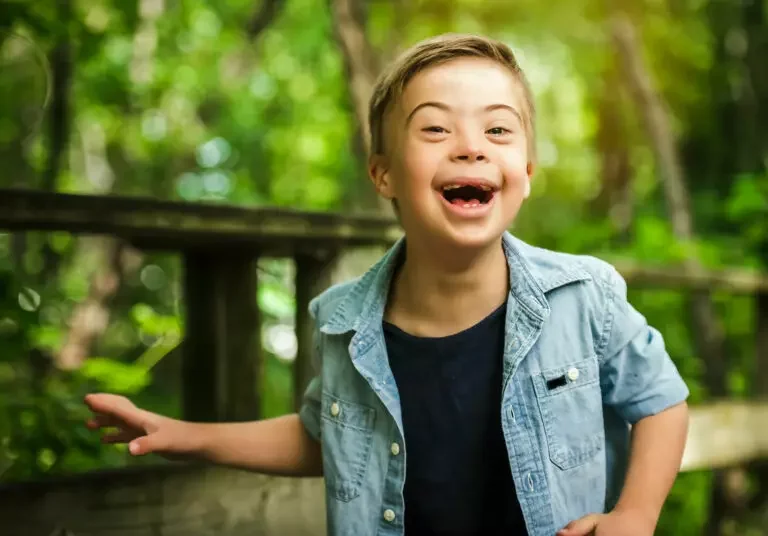 A smiling young boy outdoors among green trees
