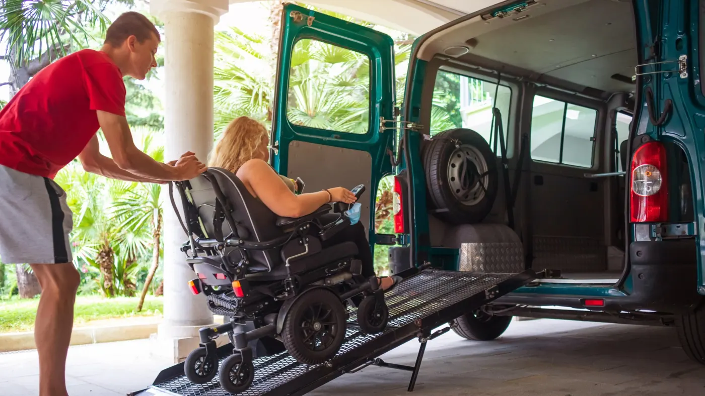 A support worker helping a woman in a power wheelchair up a van ramp