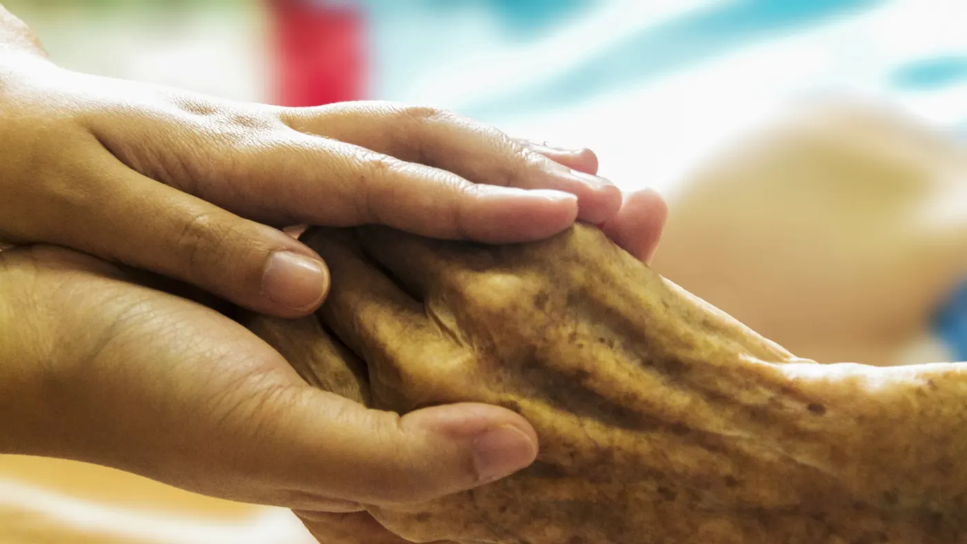 A support worker holding an older person's hand