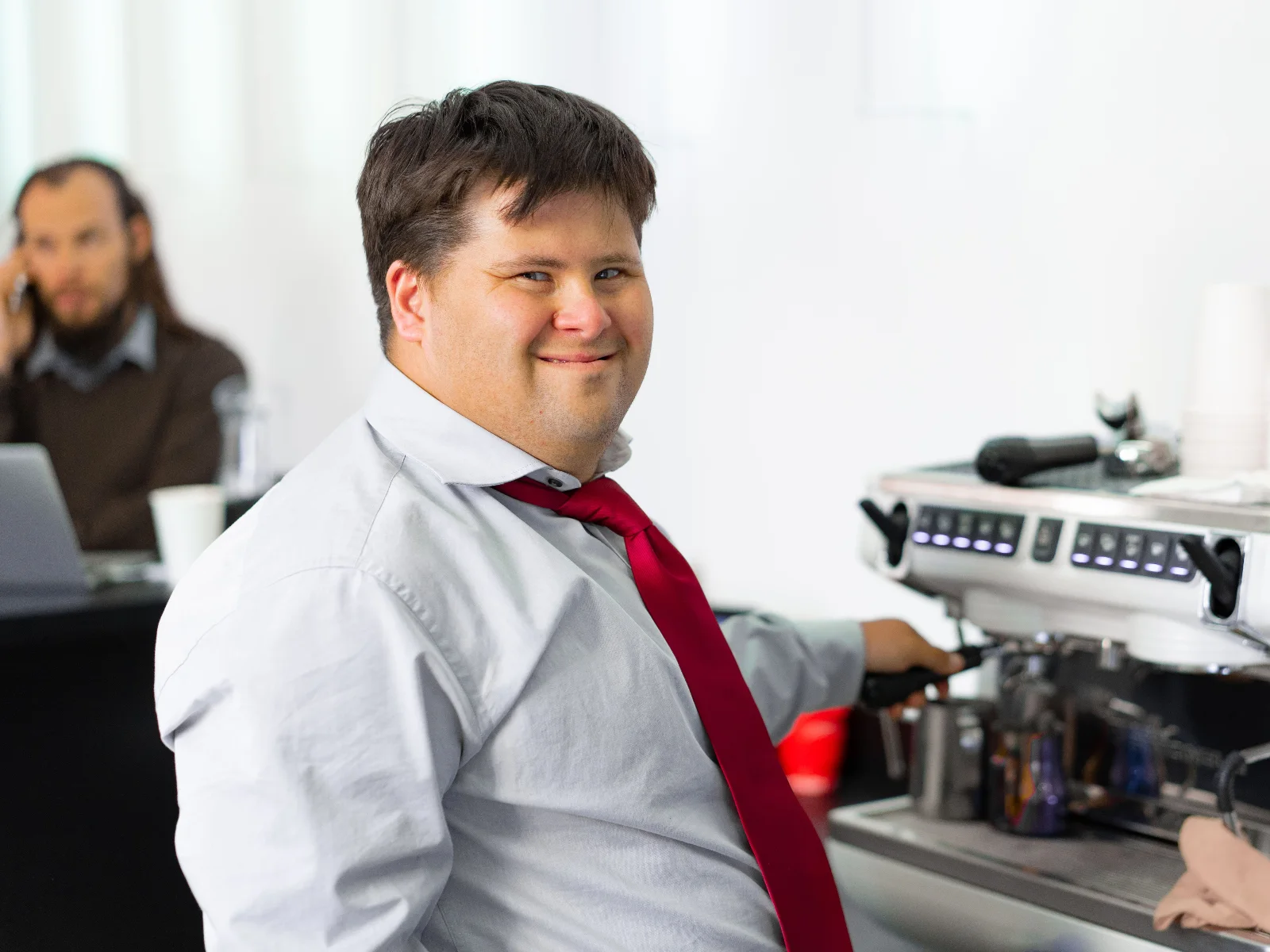 A smiling young man in a shirt and tie making coffee at a café espresso machine