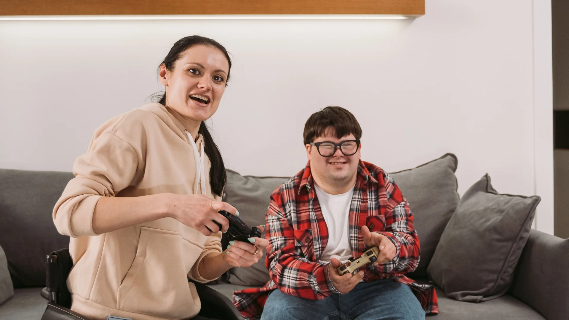Two housemates laughing while they play video games on the couch at home