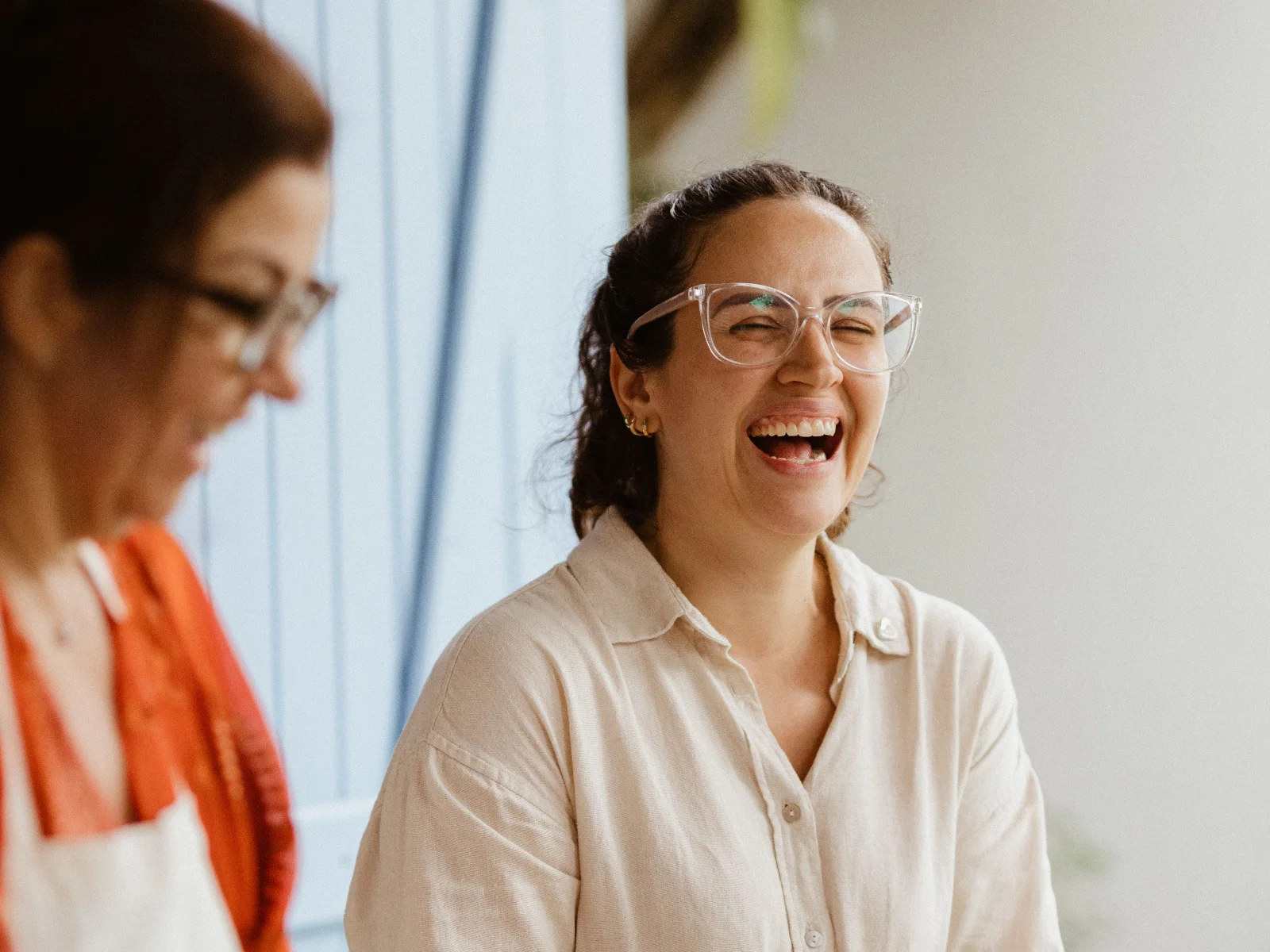 Two women laughing as they prepare food together in a bright kitchen
