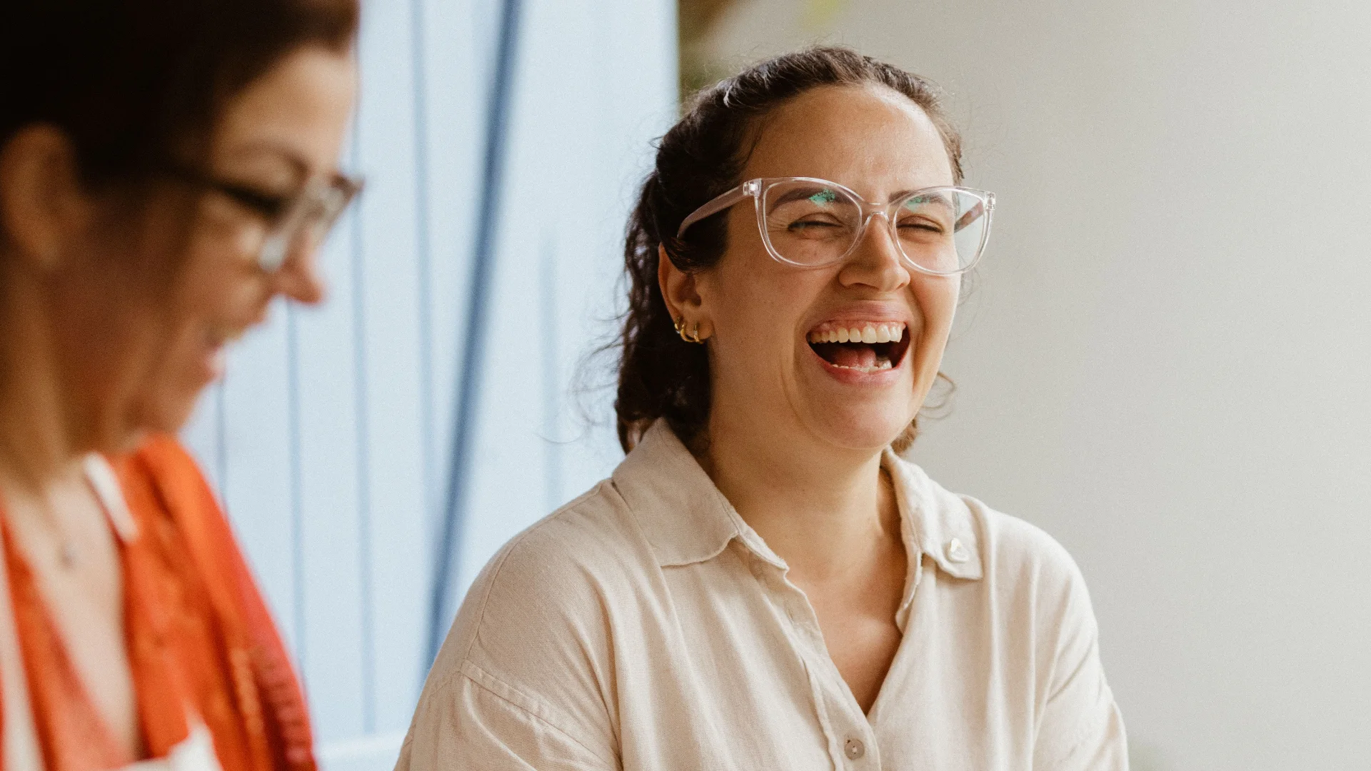 Two women laughing as they prepare food together in a bright kitchen