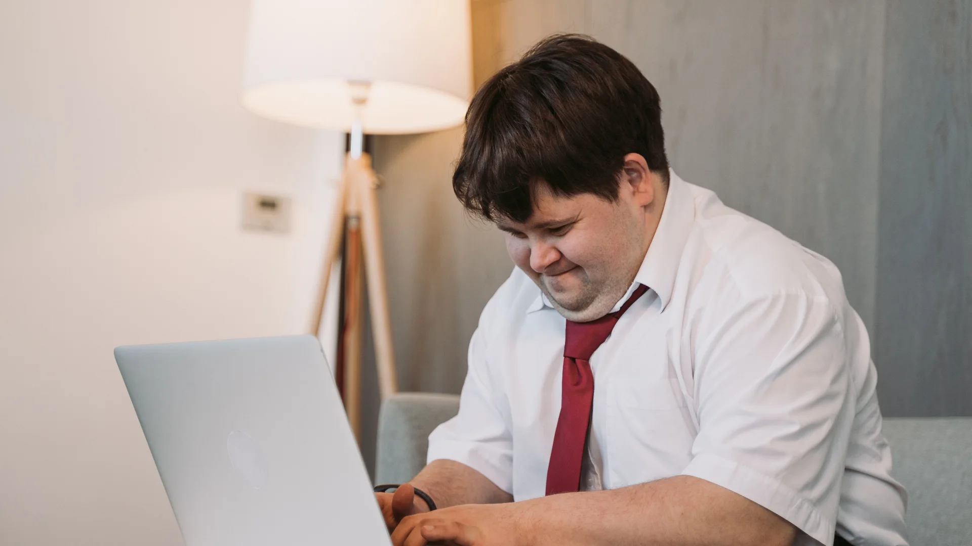 A young man in a shirt and tie reading on his laptop at home