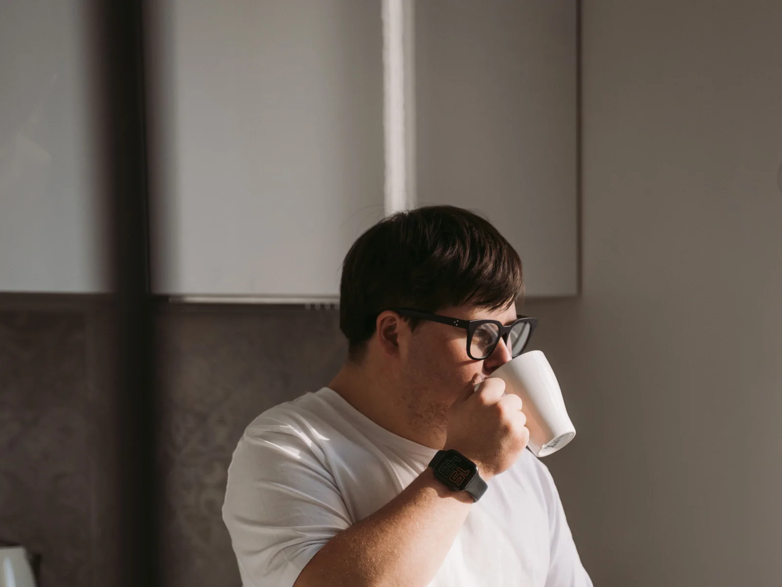 A young man in glasses enjoying his morning coffee in the kitchen