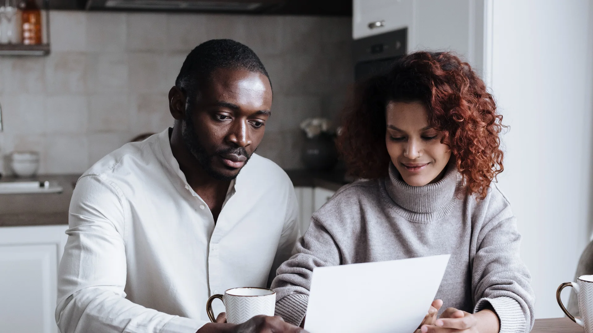 A man and a woman going through paperwork together over coffee at the kitchen table
