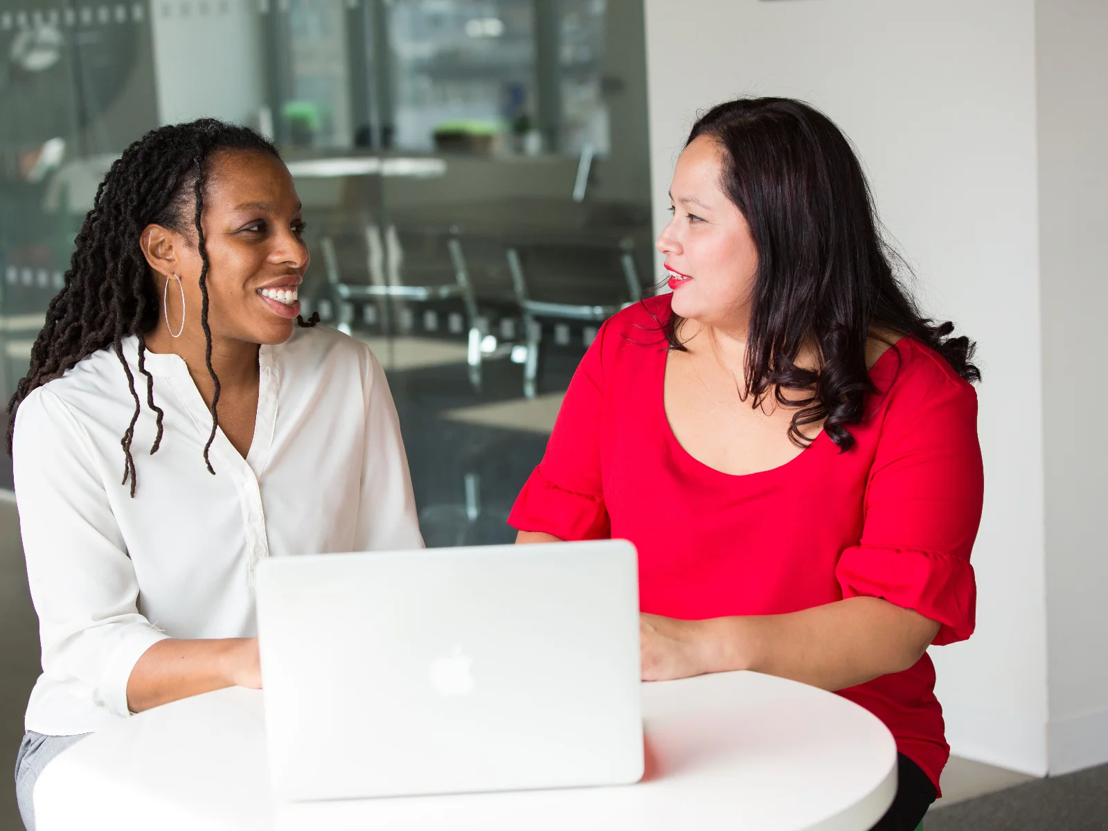 Two women smiling and talking over a laptop at a table