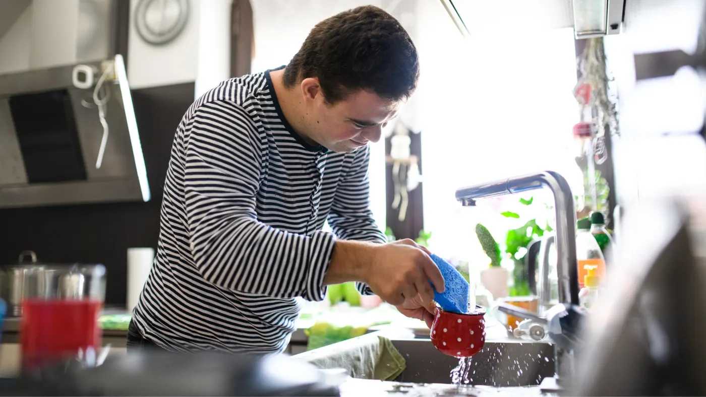 A young man washing dishes in his kitchen