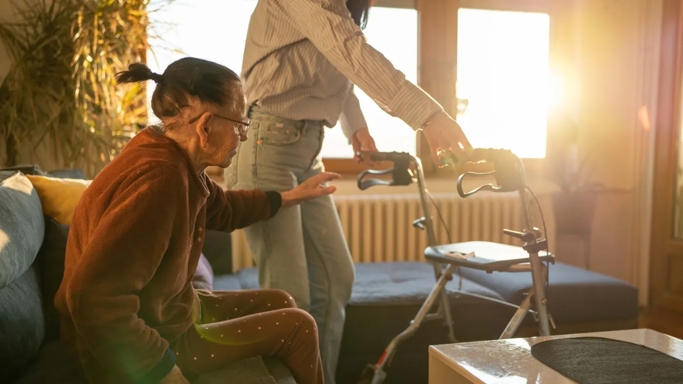 A support worker helping a woman with her walker in a sunny living room