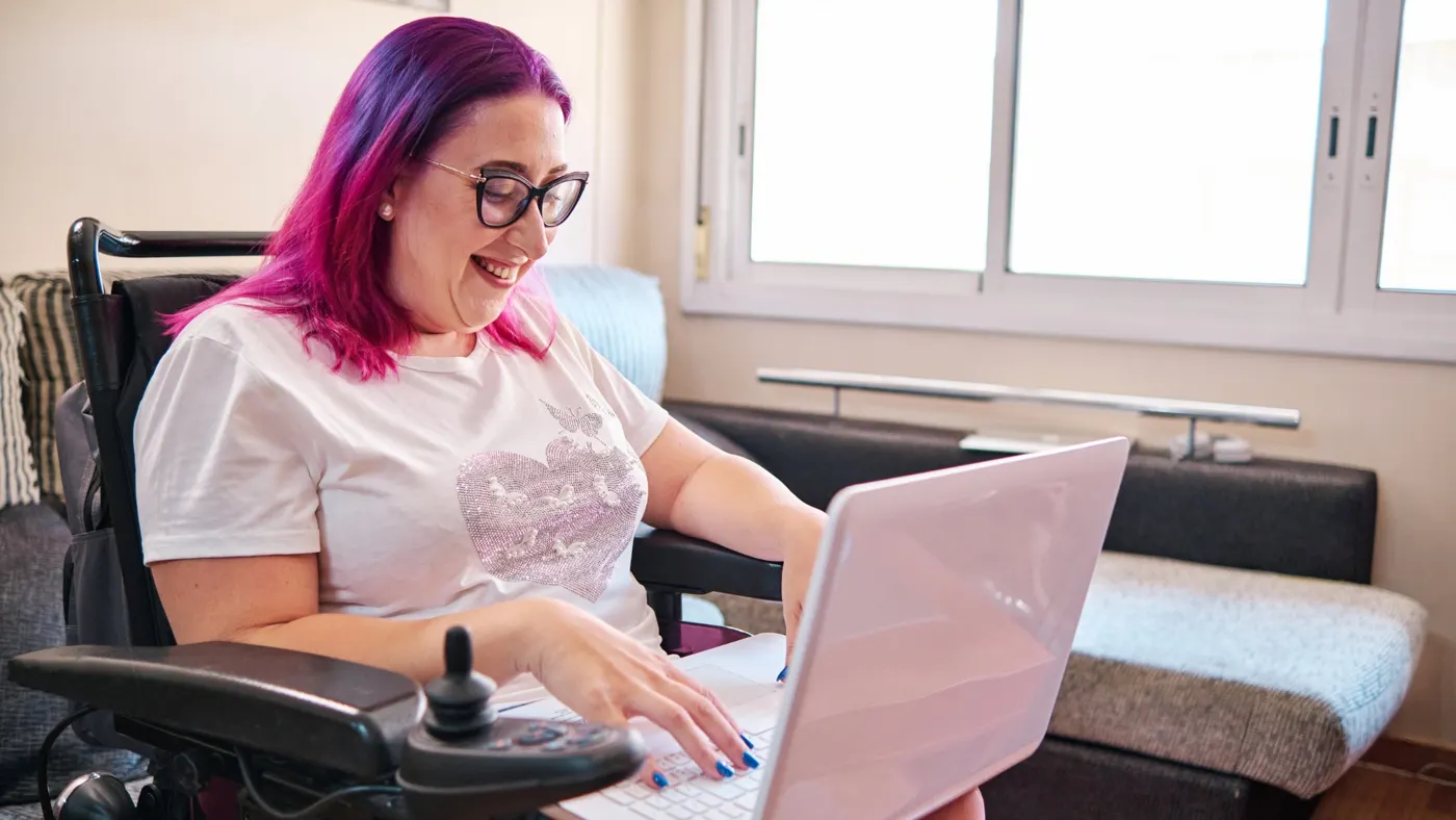 A woman in a wheelchair smiling while using her laptop at home