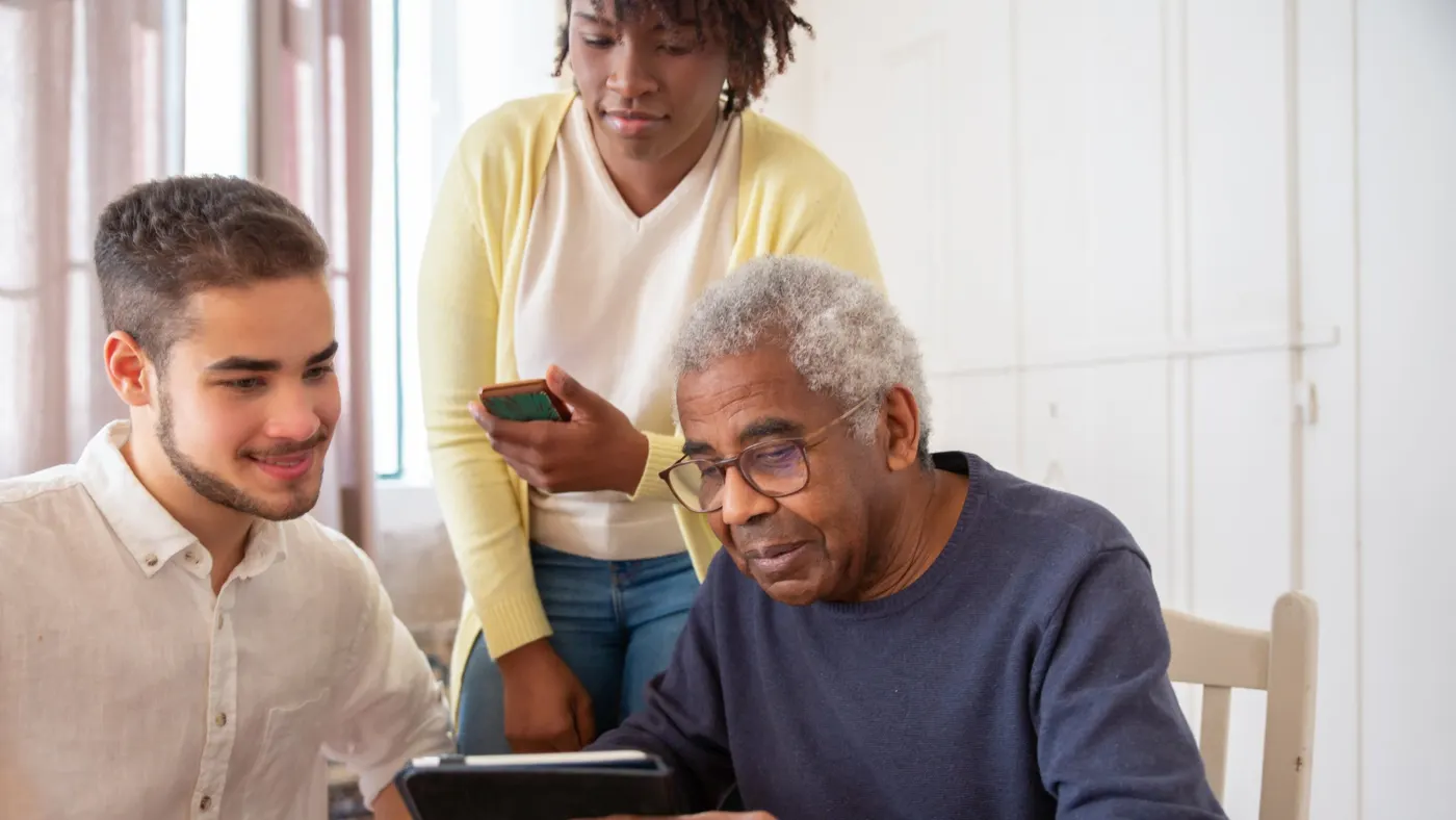 A support worker and family member helping an older man with a tablet