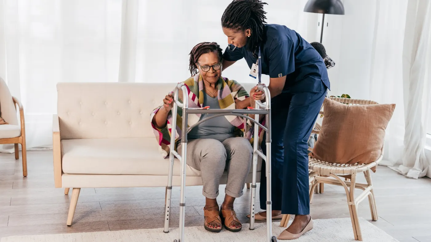 A support worker helping a woman stand with her walker at home